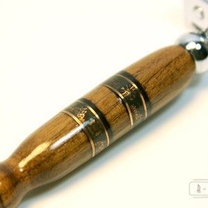 Puede incluir: Primer plano de un mango de navaja de afeitar de seguridad de madera con incrustaciones doradas y negras. El mango es de madera oscura con un acabado brillante. La cabeza de la navaja es de cromo y est&aacute; unida al mango.