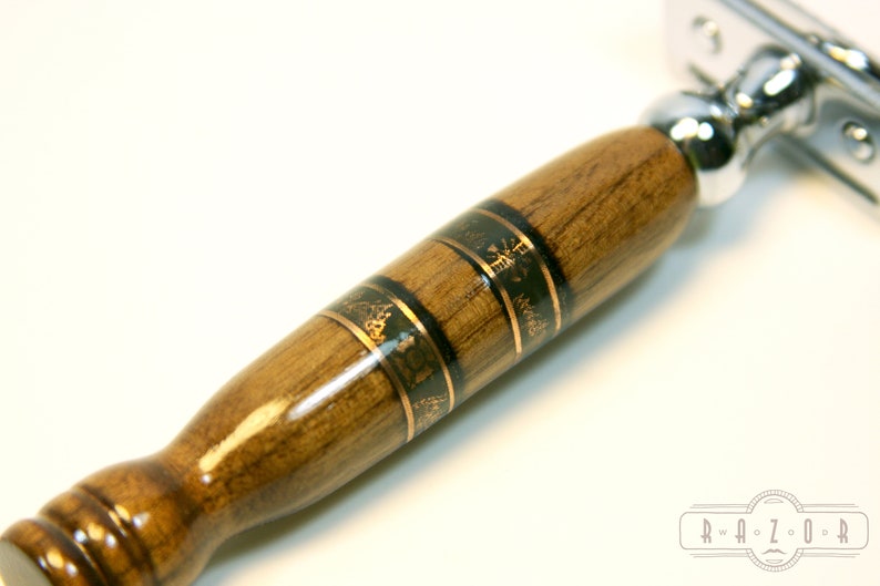 Puede incluir: Primer plano de un mango de navaja de afeitar de seguridad de madera con incrustaciones doradas y negras. El mango es de madera oscura con un acabado brillante. La cabeza de la navaja es de cromo y est&aacute; unida al mango.