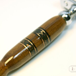 Puede incluir: Un mango de navaja de afeitar de seguridad de madera con un dise&ntilde;o de incrustaciones en negro y dorado. El mango est&aacute; hecho de madera oscura y presenta un dise&ntilde;o de hacha dorada.