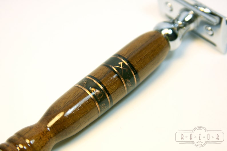 Puede incluir: Un mango de navaja de afeitar de seguridad de madera con un dise&ntilde;o de incrustaciones en negro y dorado. El mango est&aacute; hecho de madera oscura y presenta un dise&ntilde;o de hacha dorada.