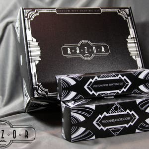 Puede incluir: Un kit de afeitado h&uacute;medo personalizado en blanco y negro con las palabras "Woodrazor.com" y "Custom Wet Shaving Kit" impresas en las cajas. El kit viene en una caja negra con un dise&ntilde;o blanco y las palabras "Woodrazor" impresas en la parte delantera.
