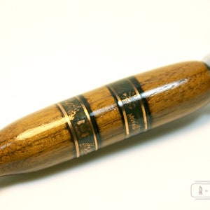 Puede incluir: Un mango de navaja de afeitar de seguridad de madera con una incrustaci&oacute;n decorativa de oro y negro. El mango es de madera oscura con un acabado liso.