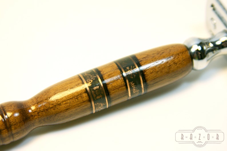 Puede incluir: Un mango de navaja de afeitar de seguridad de madera con una incrustaci&oacute;n decorativa de oro y negro. El mango es de madera oscura con un acabado liso.