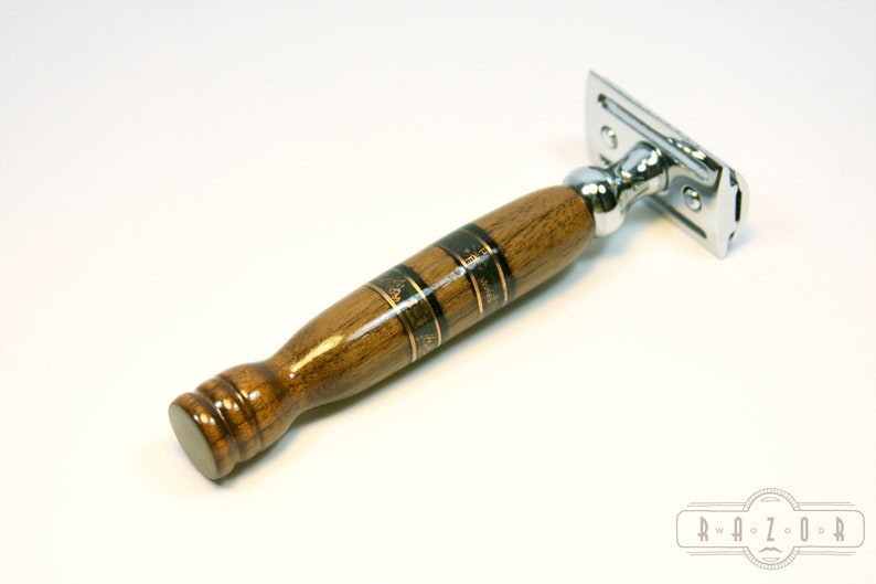 Puede incluir: Una maquinilla de afeitar de seguridad con una cabeza cromada y un mango de madera. El mango es marr&oacute;n con detalles en negro y dorado.