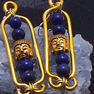 Peut inclure: Boucles d'oreilles en fil d'or avec une pierre bleue et un charme Bouddha en or. Les boucles d'oreilles sont suspendues à une roche de cristal blanche.