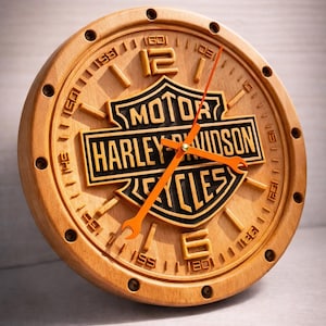 May include: A wooden clock with the Harley-Davidson logo. The clock face is light brown with orange hands and black lettering. The clock has a circular shape and is likely for wall mounting.