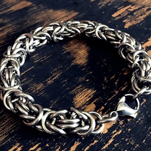 May include: A silver chain bracelet with a lobster clasp closure. The bracelet is made of interlocking metal rings.