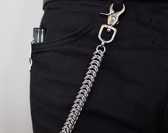 May include: A silver chain with a silver hook attached to a pair of black jeans. The chain is made of small, interlocking rings.