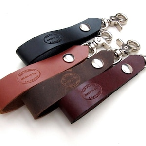 May include: Four leather keychains with metal swivel clips. Each keychain has a different color: black, brown, red, and dark brown. Each keychain has a stamped logo that reads "Dan Filipo Made in USA Leather".