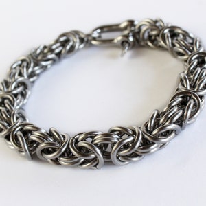 May include: A silver chain bracelet with a clasp closure. The bracelet is made of interlocking metal rings.