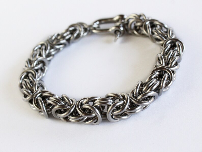 May include: A silver chain bracelet with a clasp closure. The bracelet is made of interlocking metal rings.