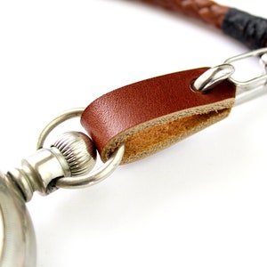 May include: A silver pocket watch with a brown leather strap and a silver chain attached to the strap.