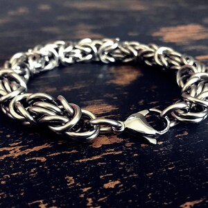 May include: A silver chain bracelet with a clasp closure. The bracelet is made of interwoven metal links.