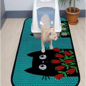 May include: A turquoise blue cat litter mat with a black cat design and red flowers. The mat has a black border and a white polka dot pattern.