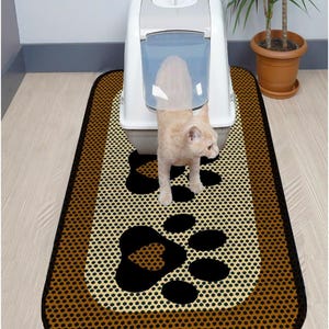 May include: A brown and beige cat litter mat with black paw prints. The mat has a textured surface and a brown border. A white cat litter box is in the background.