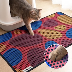 May include: A rectangular cat litter mat featuring a perforated mesh surface with a colorful pattern of large blue, yellow, and red circles on a dark red background. A small white label with the black text canico is attached to the bottom corner.
