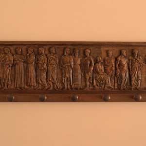 May include: A wooden coat rack with a carved relief of a procession of figures. The figures are dressed in robes and appear to be religious in nature. The rack has six hooks for hanging coats.