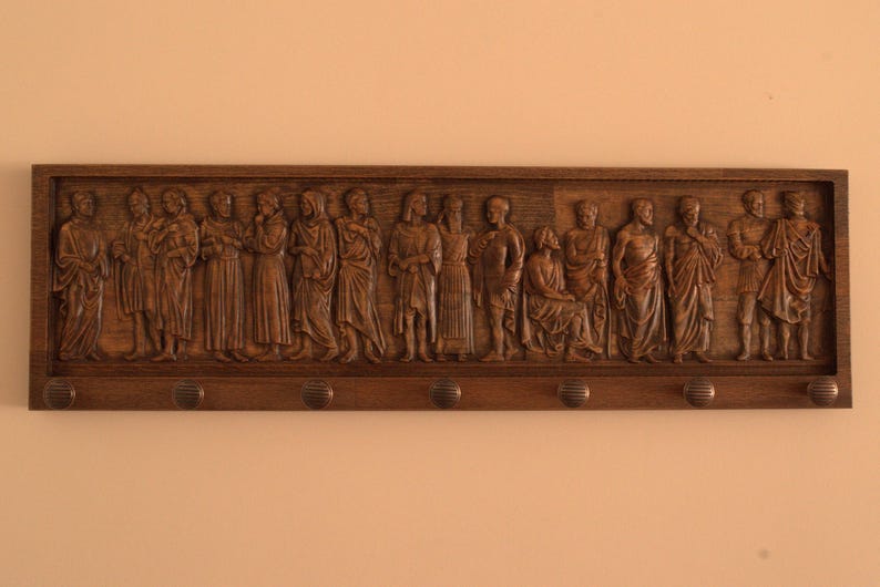 May include: A wooden coat rack with a carved relief of a procession of figures. The figures are dressed in robes and appear to be religious in nature. The rack has six hooks for hanging coats.