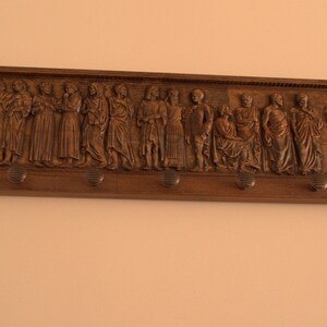 May include: A wooden wall-mounted coat rack with a carved design of people. The rack has five hooks.