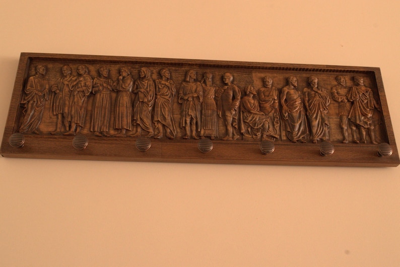 May include: A wooden wall-mounted coat rack with a carved design of people. The rack has five hooks.
