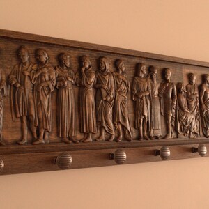 May include: A wooden wall-mounted coat rack with a carved relief of figures. The rack has 10 hooks and is stained a dark brown.