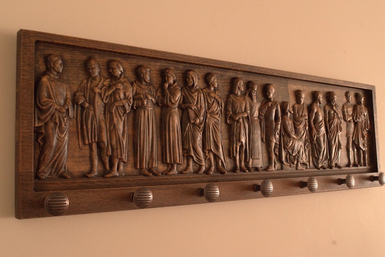 May include: A wooden wall-mounted coat rack with a carved relief of figures. The rack has 10 hooks and is stained a dark brown.