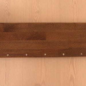 May include: A dark brown wooden shelf with silver metal brackets on each end. The shelf has several small silver screws along the bottom edge.