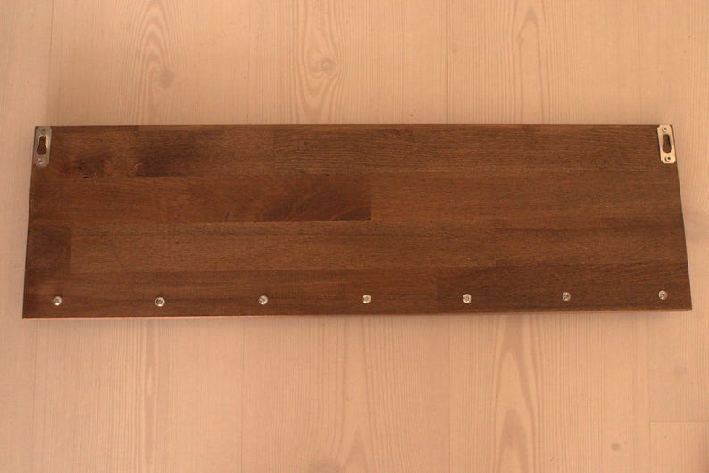 May include: A dark brown wooden shelf with silver metal brackets on each end. The shelf has several small silver screws along the bottom edge.