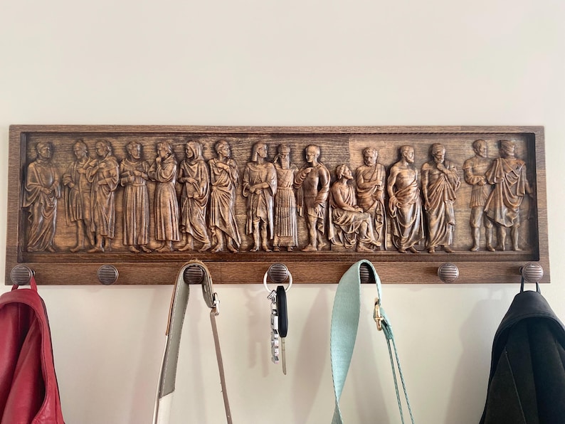 May include: A wooden coat rack with a carved relief of figures in a procession. The rack has multiple hooks for hanging coats, bags, or keys.
