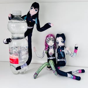 May include: A clear plastic water bottle with a white cap is embraced by a plush doll. Two further plush dolls are seated below. The dolls are anime-style characters with detailed facial features and colourful outfits.