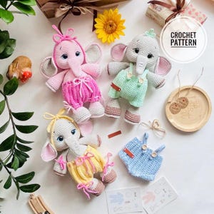 May include: Handmade crochet elephant dolls in various colours, including pink, green, and yellow. Each elephant has a unique outfit and bow. The dolls have grey and pink ears, trunks, and feet. One doll wears a mint green outfit, another a pink outfit, and the third a yellow outfit.
