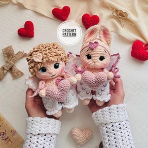 Op de afbeelding: Twee gehaakte poppen, een engel en een konijn, die elk een roze hart vasthouden. De engel heeft krullend haar en blauwe ogen. Het konijn heeft lange oren en een hart op zijn hoofd. Rode en roze gehaakte harten omringen de poppen. De tekst "CROCHET PATTERN" staat in een cirkel.