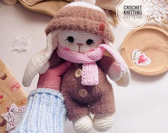 Puede incluir: Muñeca de conejo de ganchillo hecha a mano con sombrero marrón, mono y bufanda rosa. La muñeca tiene orejas y pies blancos. La imagen incluye el texto "CROCHET KNITTING PATTERN".