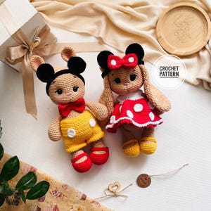 May include: Two crocheted bunny dolls, one in yellow shorts and a red bow tie, the other in a red polka dot dress and a red bow. Both dolls have black ears and are handmade. The image includes the text "CROCHET PATTERN".