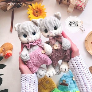 Peut inclure: Deux poupées chats crochetées à la main. L'une porte une tenue rose, l'autre une tenue marron. Les deux poupées ont une tête grise, des oreilles blanches et des yeux bleus. Les poupées sont tenues dans les mains d'une personne. L'image comprend également un tournesol et les mots "CROCHET PATTERN".