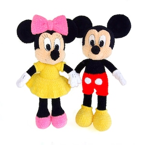 Puede incluir: Dos muñecos de crochet hechos a mano, Minnie Mouse y Mickey Mouse, están uno al lado del otro. Minnie lleva un vestido amarillo y un lazo rosa. Mickey lleva pantalones cortos rojos. Ambos tienen orejas negras, cuerpos negros y guantes blancos.