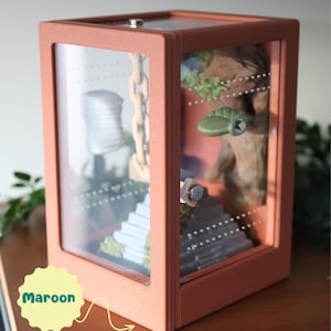 Side view of a matte green 3D-printed jumping spider enclosure, showing ventilation vents on sides and top edge, with natural moss and integrated decorative elements