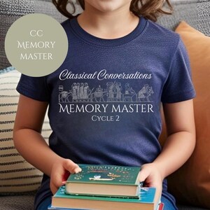 Op de afbeelding: Een marineblauw t-shirt met witte tekst "Classical Conversations Memory Master Cycle 2". Het shirt heeft een lijntekening van mensen en dieren. De persoon houdt een stapel boeken vast.