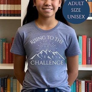 May include: A blue heather t-shirt with a white graphic of mountains and the text "Rising to the Challenge". The shirt is adult size and unisex.