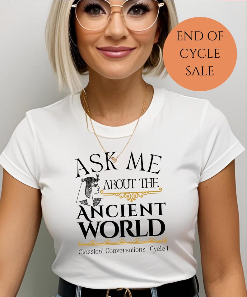 May include: White t-shirt with black text that reads "Ask Me About The Ancient World" with a stylized image of an Egyptian woman. Below the text is "Classical Conversations Cycle 1". The image has a peach colored circle with the text "End of Cycle Sale" in black.