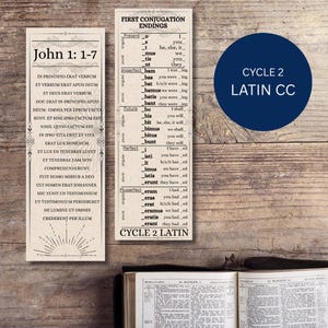 Puede incluir: Dos marcadores de color crema con texto negro. Uno presenta el texto "John 1: 1-7" y versículos latinos. El otro enumera las conjugaciones verbales latinas. Un círculo azul con "CYCLE 2 LATIN CC" está en el fondo.