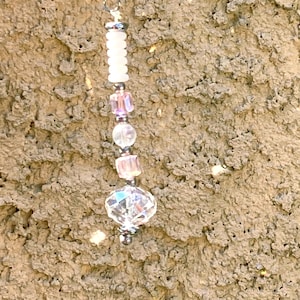 May include: A beaded keychain with a silver-tone metal clasp. The keychain features a series of beads in white, pink, and clear crystal. The beads are various shapes and sizes, creating a decorative accessory.