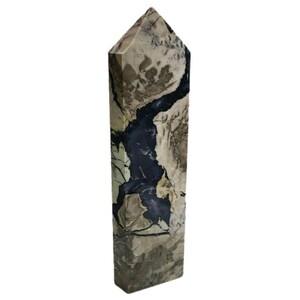 Puede incluir: Un obelisco de piedra rectangular y alto con una parte superior puntiaguda. La piedra presenta una mezcla de colores beige, gris y negro, con un prominente patrón oscuro en forma de veta que recorre el centro. El obelisco es un objeto decorativo.