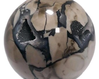 May include: A polished sphere of Septarian stone, featuring a mix of tan, gray, and black patterns. The sphere has a geode cavity with visible crystal formations. The stone is smooth and reflective, with a natural, earthy aesthetic.