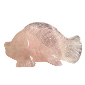 May include: A carved rose quartz fish figurine. The fish is light pink with detailed scales and fins. The sculpture is a decorative item, likely for display or collection.
