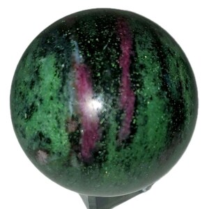 Puede incluir: Una esfera pulida de piedra verde y negra con vetas magenta. La piedra preciosa tiene un acabado brillante y un patrón moteado. La esfera es probablemente un artículo decorativo o de colección.