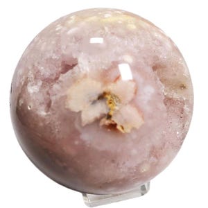 May include: A spherical, polished gemstone in shades of pink and white, with a geode-like cavity revealing crystalline formations. The sphere is supported by a clear acrylic stand, showcasing its natural beauty. The stone has a flower-like pattern.