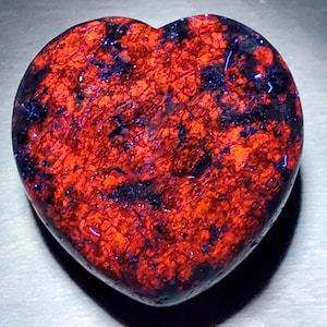 May include: A heart-shaped stone featuring a striking red and black mottled design. The polished surface catches the light, emphasizing the natural colour and texture variations. This decorative item could be used as a paperweight or a unique gift.
