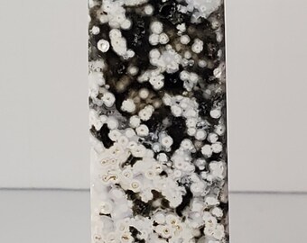 May include: A tall, rectangular stone obelisk with a flat top. The stone features a pattern of white, cream, and black spots and swirls. The obelisk is a decorative item.