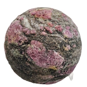 Könnte beinhalten: Ein kugelförmiger Stein mit rauer Textur, der eine Mischung aus dunkelgrauen, hellgrauen und rosaroten Mineralablagerungen aufweist. Die Oberfläche des Steins ist uneben, mit den rosa Mineralien in Clustern.